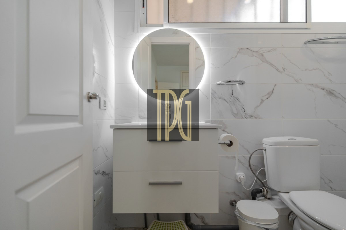 Circular backlit mirror above a white two-drawer vanity in a modern marble-tiled bathroom