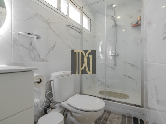 Modern bathroom with glass shower enclosure, marble walls, a sink vanity, and toilet.