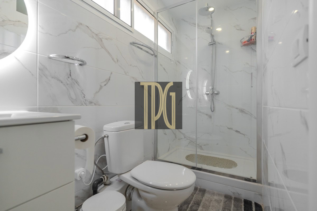 Modern bathroom with glass shower enclosure, marble walls, a sink vanity, and toilet.