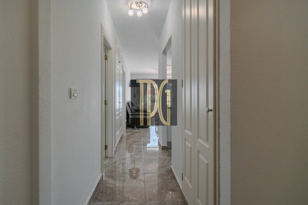 Bright hallway in a home with white walls and marble floor, opening to a living area with a sofa in the distance.