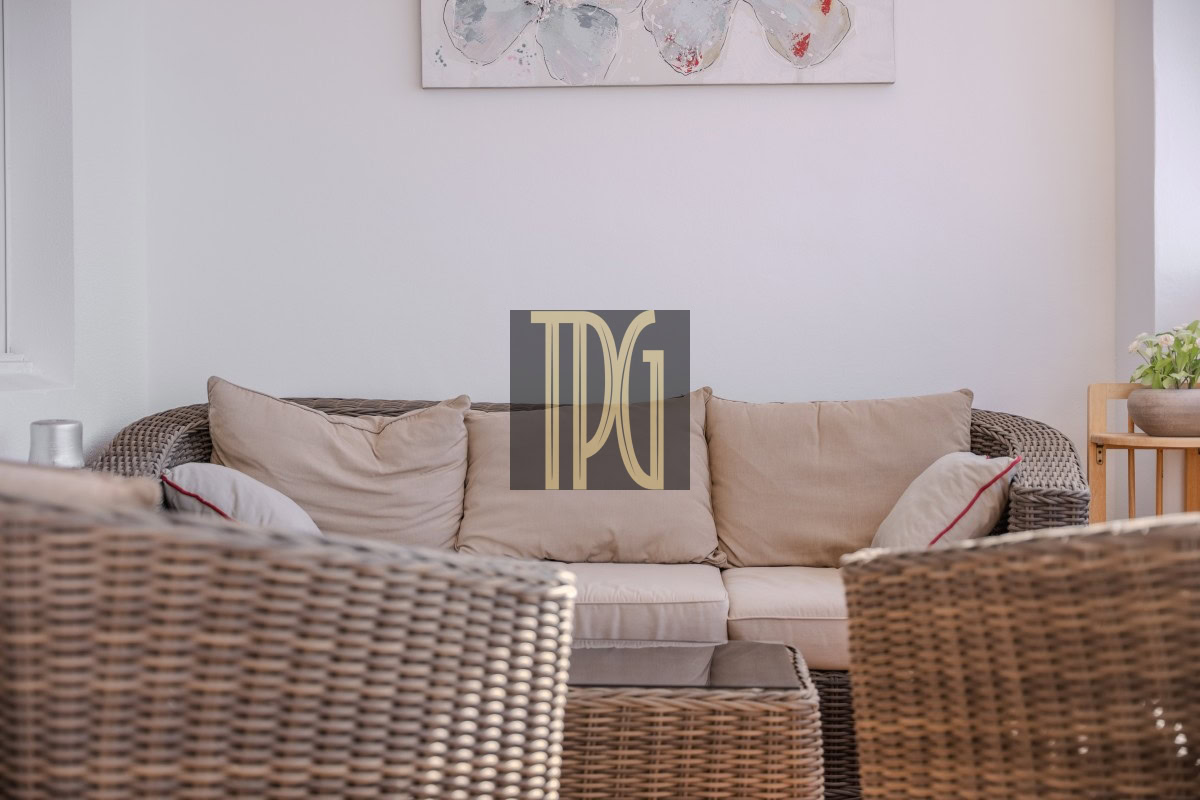 Cozy wicker sofa set with beige cushions in a bright living room, with a glass coffee table and a potted plant on the side table.