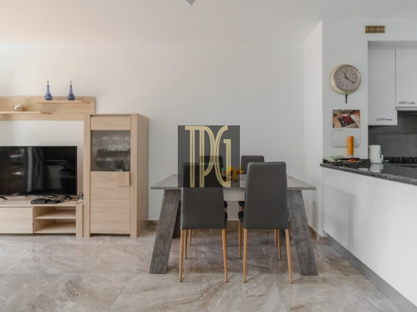 Open-plan living and dining area with a wooden TV cabinet, mounted TV, concrete-look dining table, and four gray chairs around it.