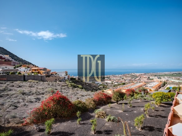 Coastal hillside town with red-roofed houses, overlooking the sea under a clear blue sky.