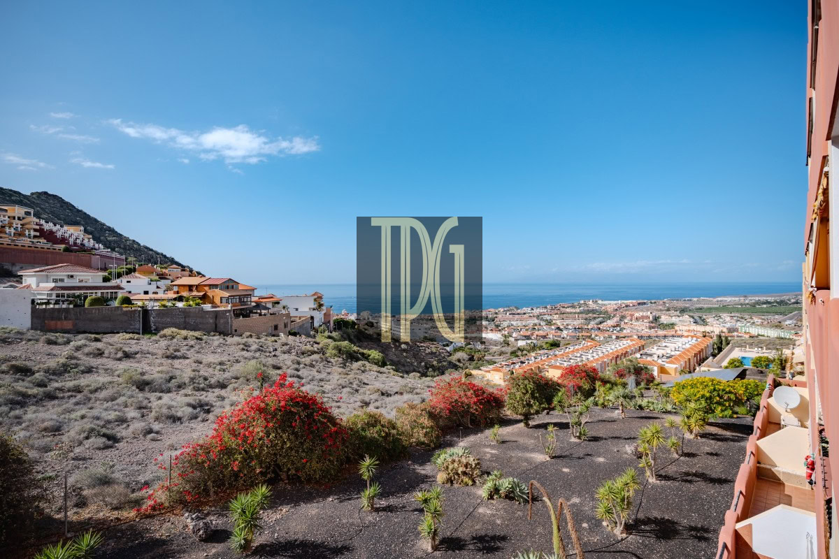 Coastal hillside town with red-roofed houses, overlooking the sea under a clear blue sky.