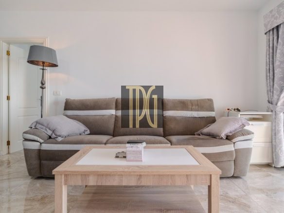 Bright living room with a beige sectional sofa, light wood coffee table, floor lamp on the left, and patterned curtains on the right.