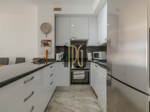 Modern white kitchen with granite countertops, built-in oven, microwave, and stainless fridge; wall clock and calendar above the counter.