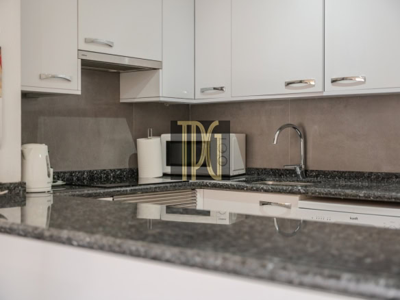 Modern kitchen workspace with white cabinets, gray granite counter, sink, and small appliances like a kettle and microwave on the counter.