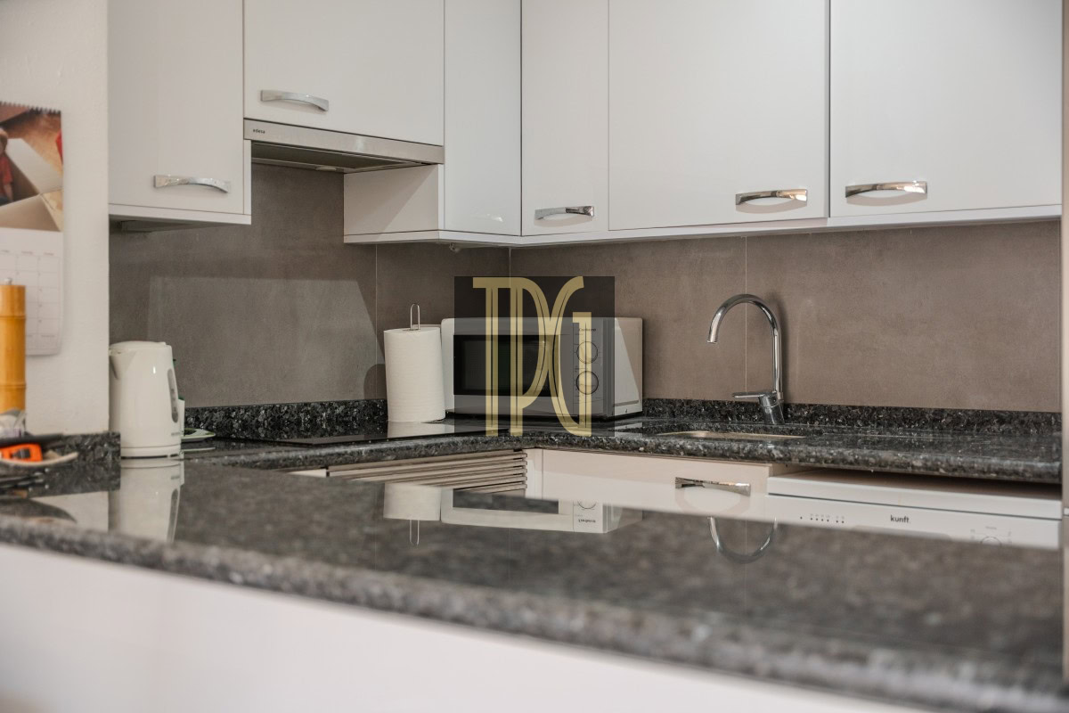 Modern kitchen workspace with white cabinets, gray granite counter, sink, and small appliances like a kettle and microwave on the counter.