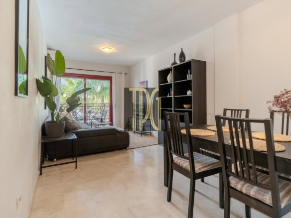 Open-plan living and dining room: dark sofa, tall black bookshelf, and a six-seat dining table, with a balcony door at the back.