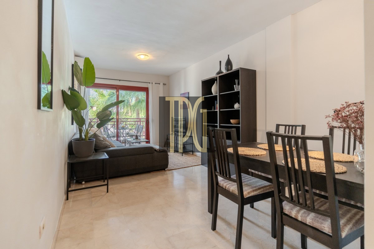 Open-plan living and dining room: dark sofa, tall black bookshelf, and a six-seat dining table, with a balcony door at the back.