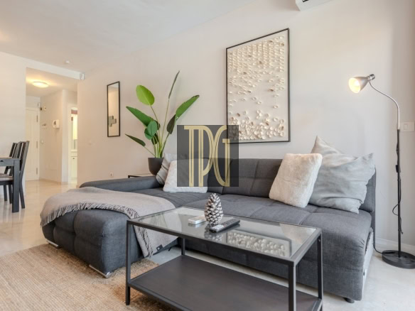 Modern living room with a dark gray sectional sofa, glass coffee table, and a tall floor lamp by the wall art. A potted plant and beige throw pillows complete the space.