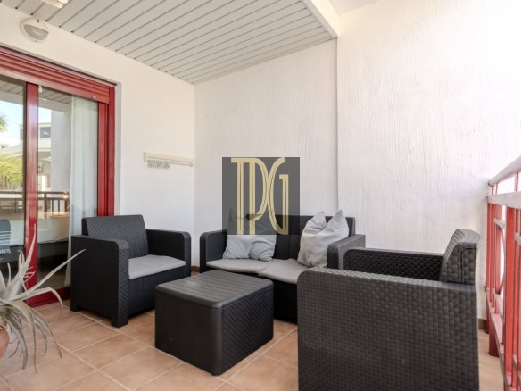 Outdoor balcony seating area with black wicker sofa and chairs, gray cushions, and a red-framed glass door.