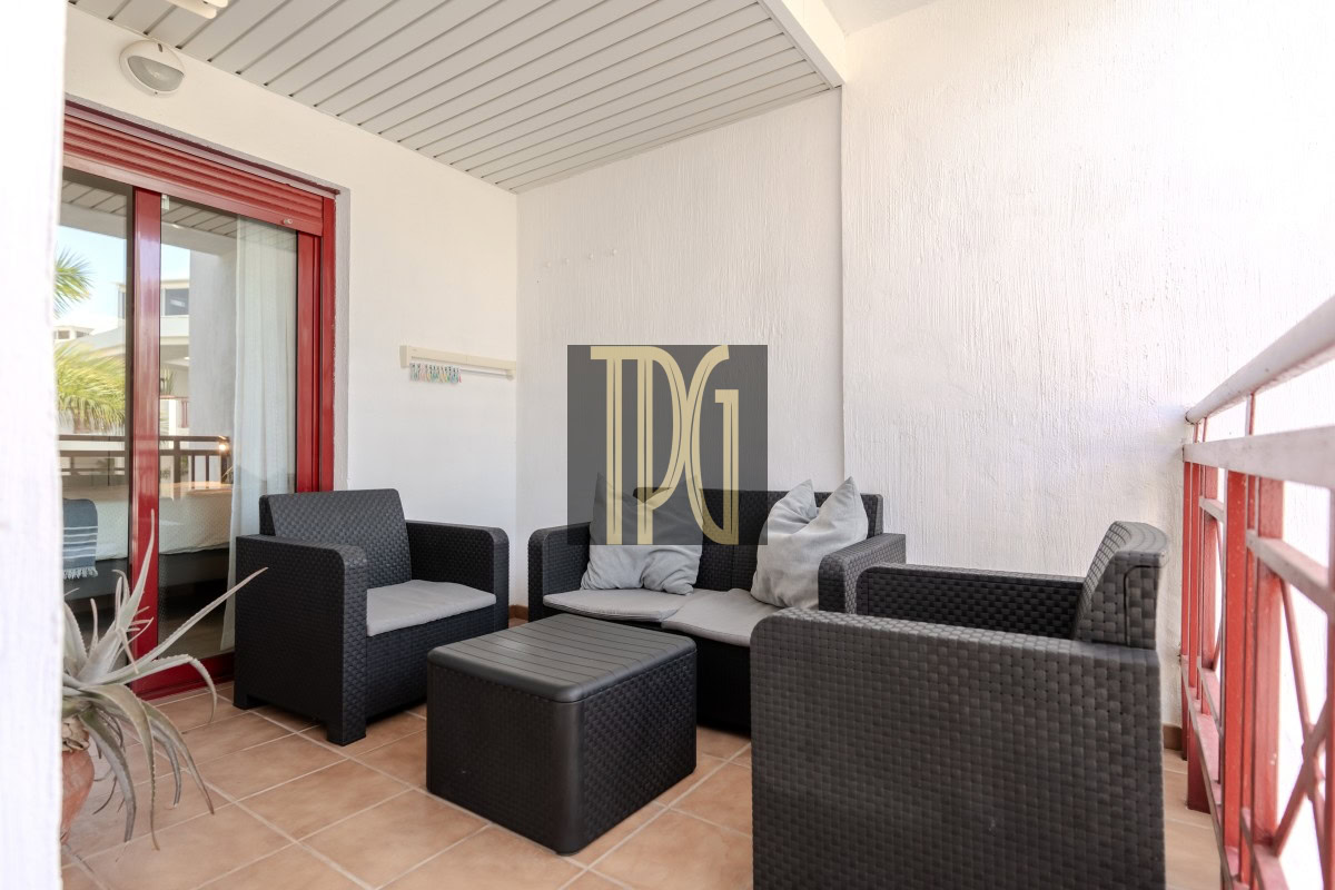 Outdoor balcony seating area with black wicker sofa and chairs, gray cushions, and a red-framed glass door.