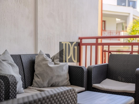 Outdoor balcony seating area with dark wicker sofa and chairs, light gray cushions, and a red railing in the background