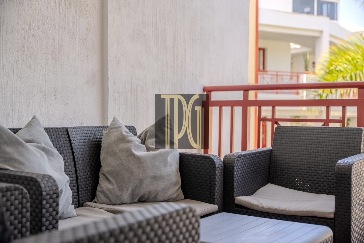 Outdoor balcony seating area with dark wicker sofa and chairs, light gray cushions, and a red railing in the background