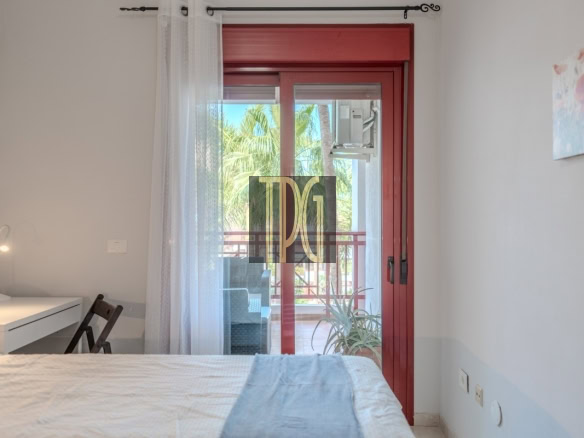 Bedroom with a red-framed glass door opening to a balcony, a white desk and lamp on the left.