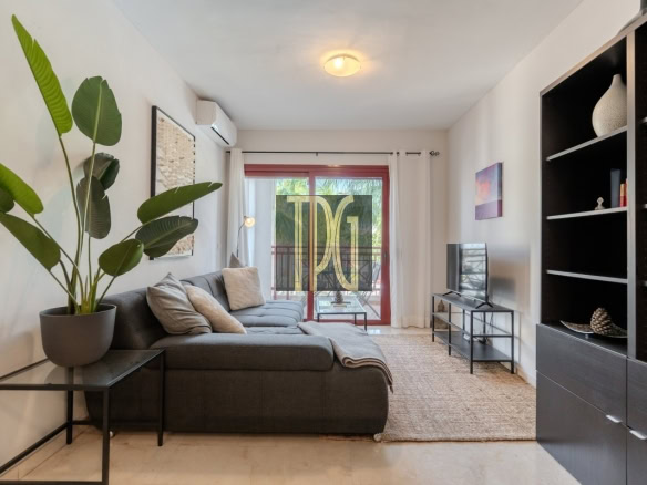 Modern living room with a gray L-shaped sofa, beige cushions, and a large potted plant near a glass balcony door with a red frame.