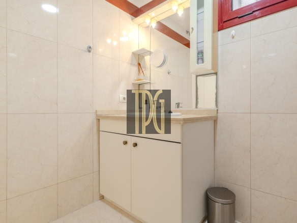 Bathroom vanity with beige countertop, white cabinets, and a mirror in a tiled room