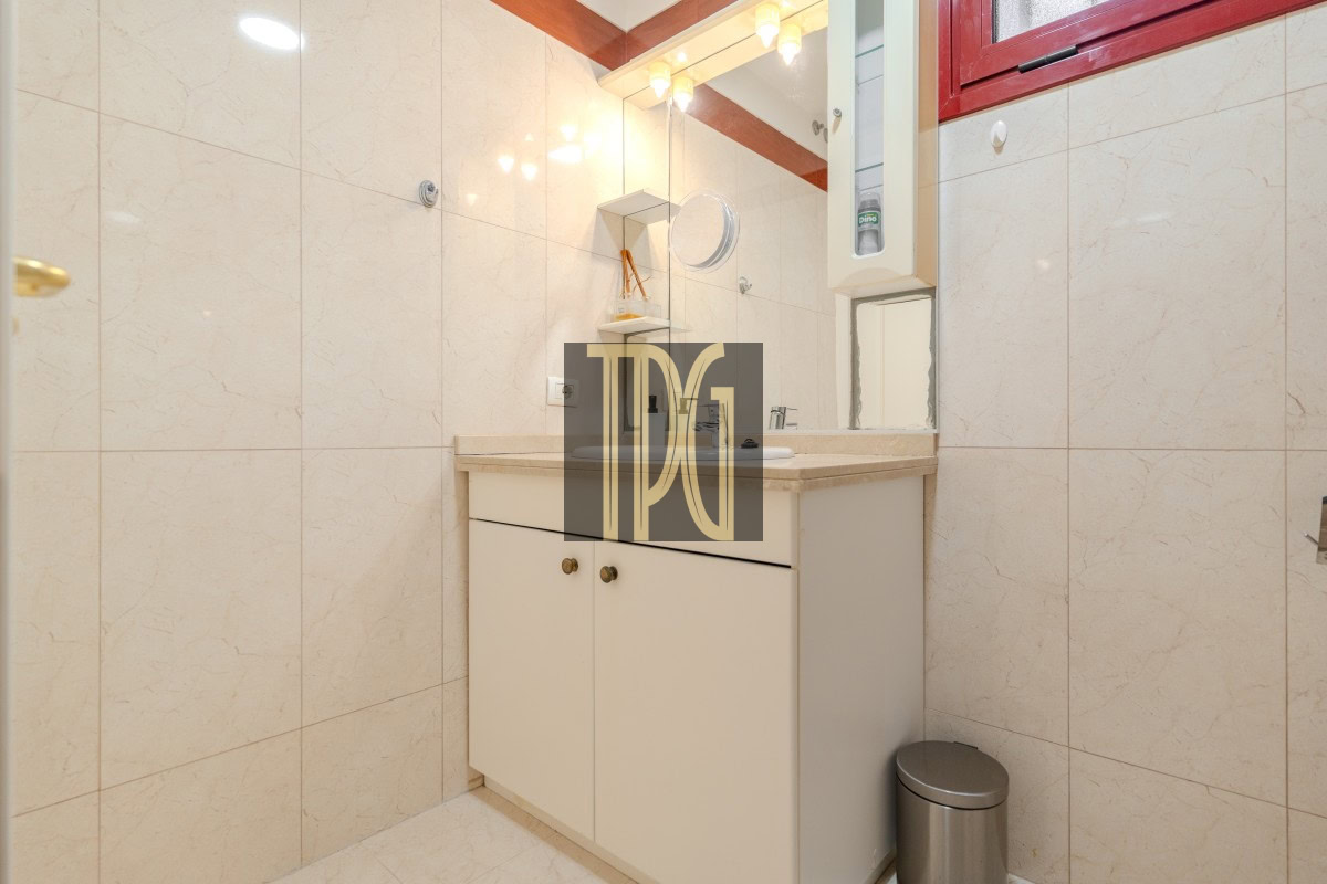 Bathroom vanity with beige countertop, white cabinets, and a mirror in a tiled room