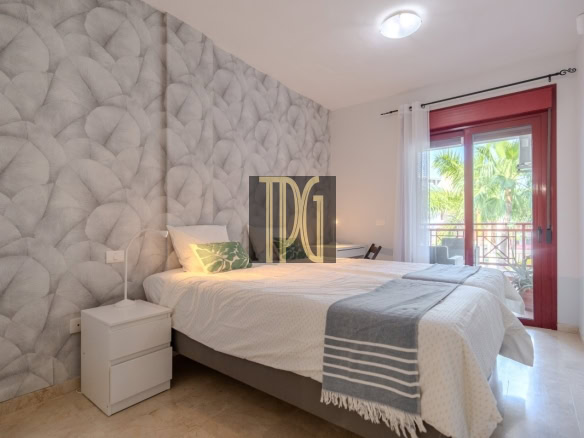 Cozy double bedroom with a textured gray feature wall, white bedding, and a balcony door with a red frame.
