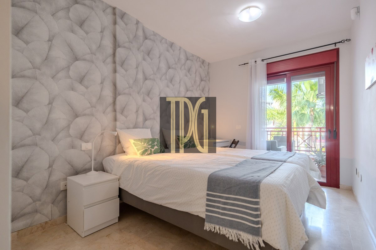 Cozy double bedroom with a textured gray feature wall, white bedding, and a balcony door with a red frame.
