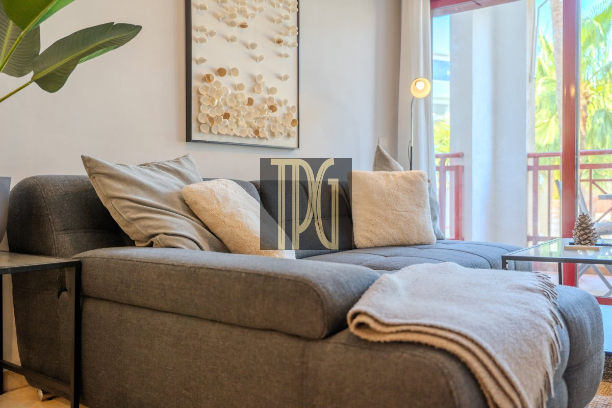 Cozy modern living room with a gray sectional, cream pillows, and a beige throw blanket on a glass coffee table nearby, plus a potted plant and wall art.