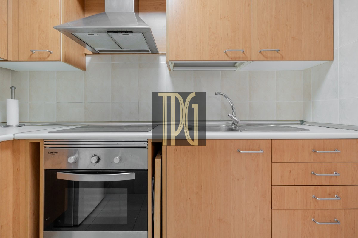 Modern kitchen with wood cabinets, stainless oven, and a double sink along a tiled backsplash on white counter.