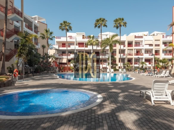 Resort courtyard with circular pool in foreground, rectangular pool beyond, white buildings with red railings, and palm trees.