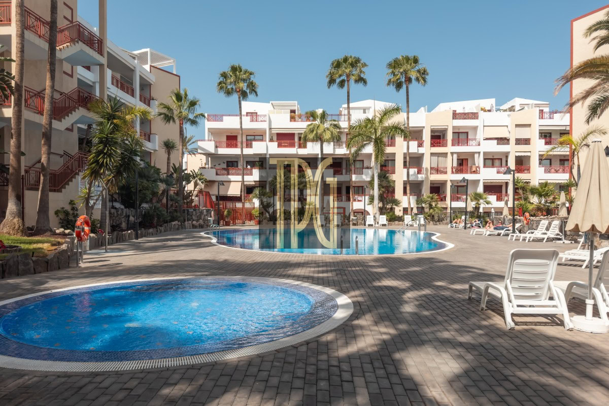 Resort courtyard with circular pool in foreground, rectangular pool beyond, white buildings with red railings, and palm trees.