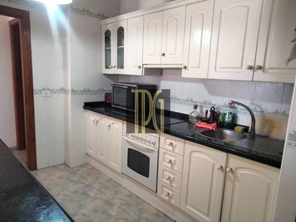 Compact kitchen with white paneled cabinets, black countertop, built-in oven, and stainless sink.