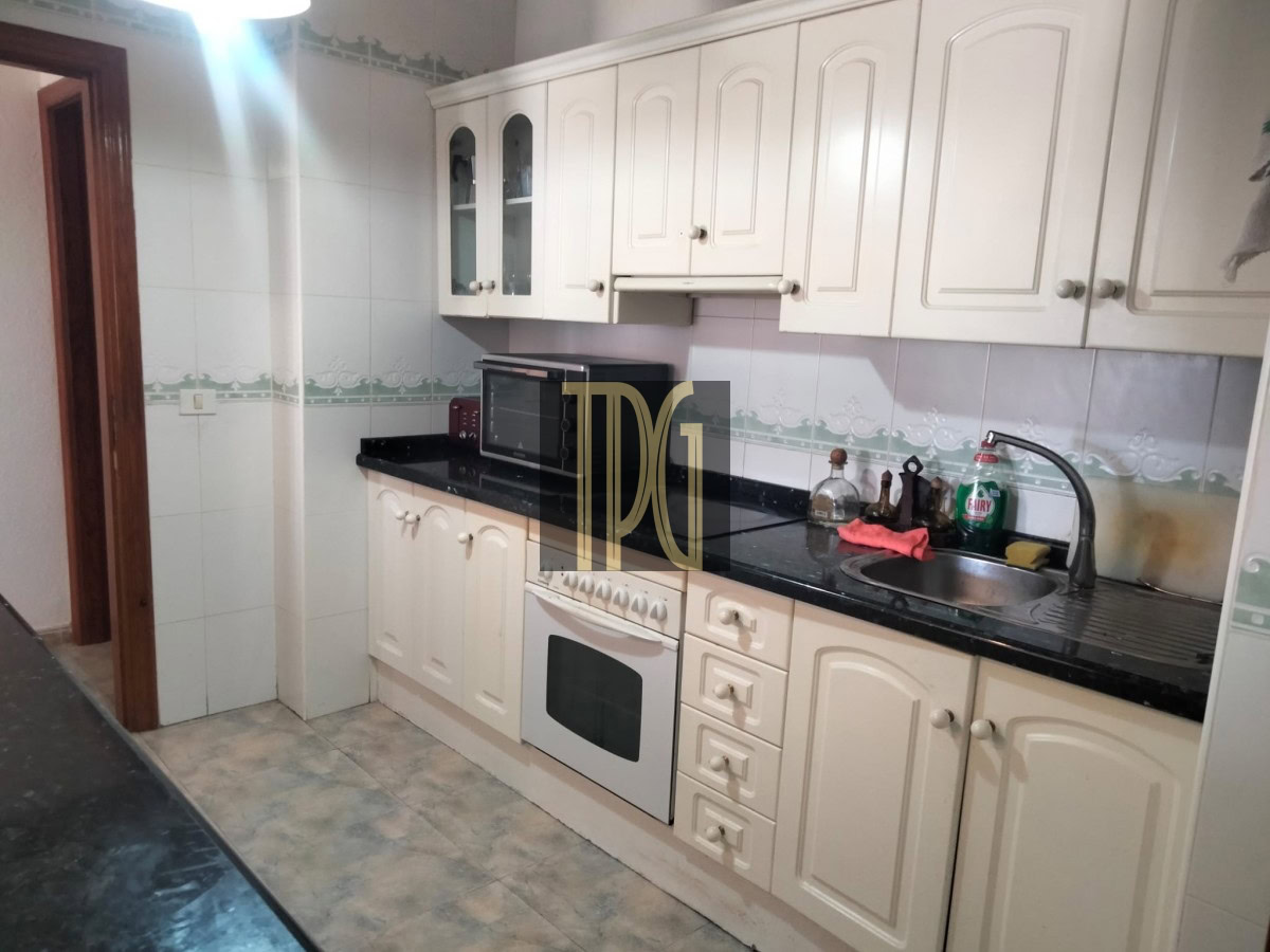 Compact kitchen with white paneled cabinets, black countertop, built-in oven, and stainless sink.