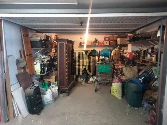 Cluttered garage/storage space packed with boxes, bags, furniture, and a shopping cart.