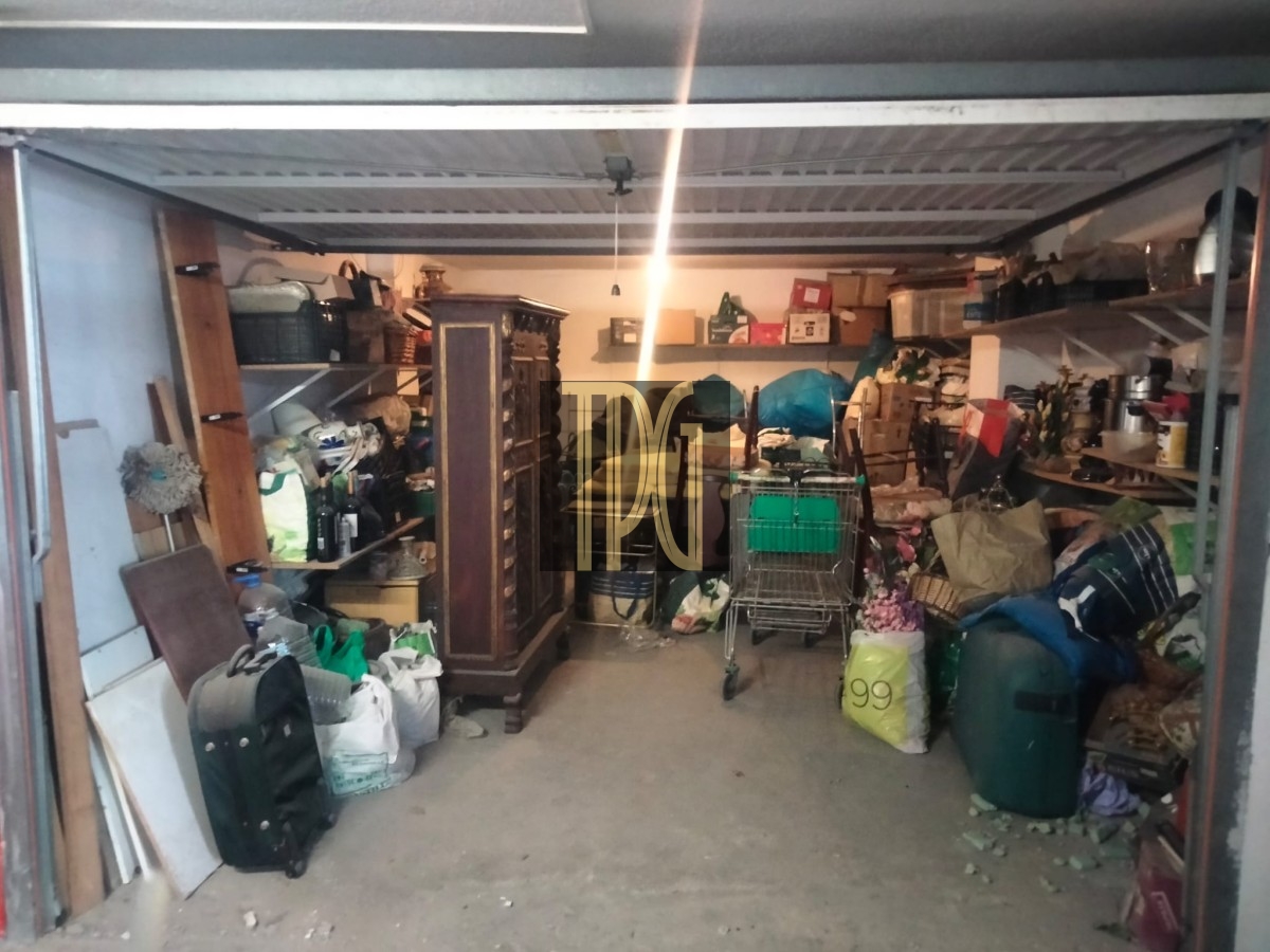 Cluttered garage/storage space packed with boxes, bags, furniture, and a shopping cart.