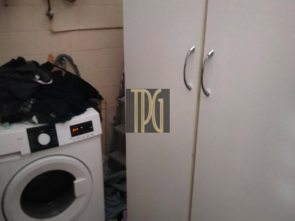 Laundry room with a front-loading washing machine, a pile of clothes on top, and white wardrobes with silver handles.