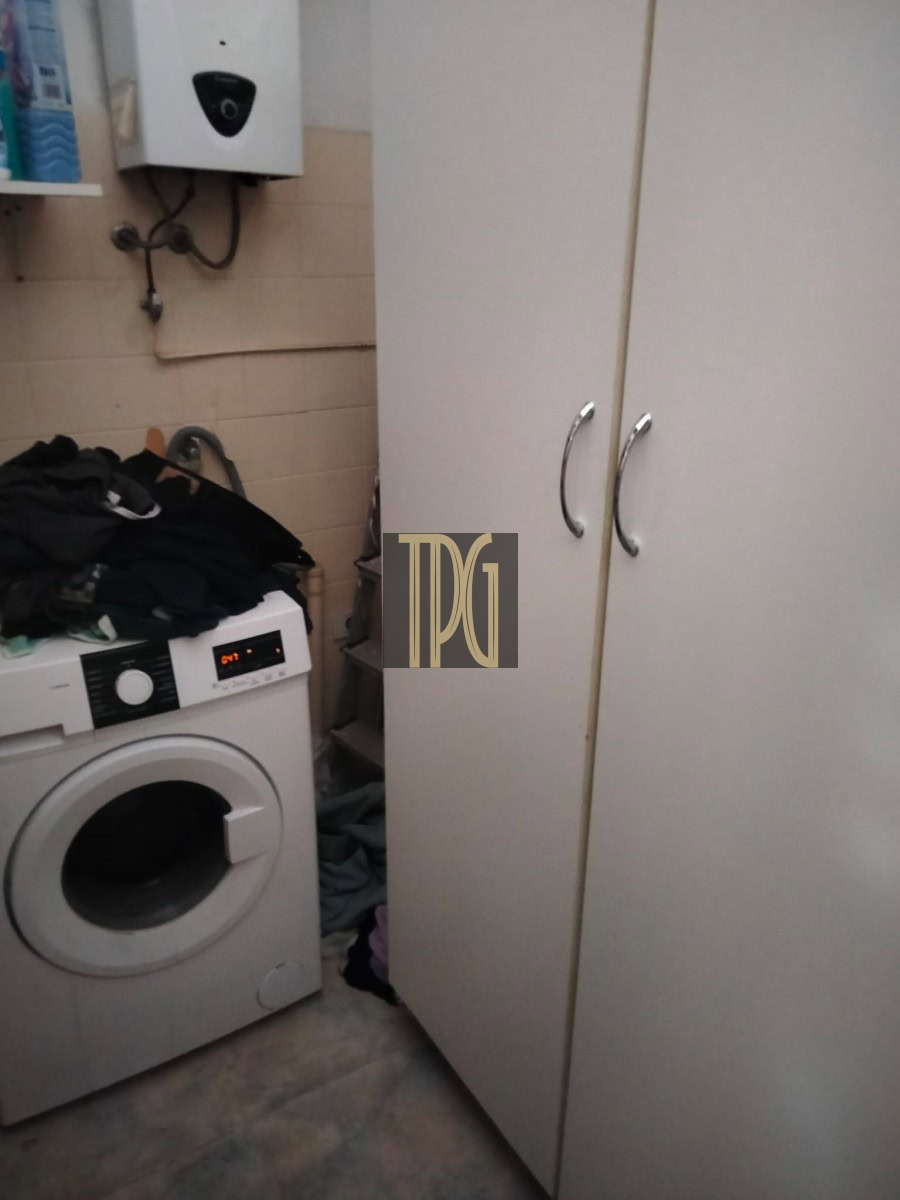 Laundry room with a front-loading washing machine, a pile of clothes on top, and white wardrobes with silver handles.