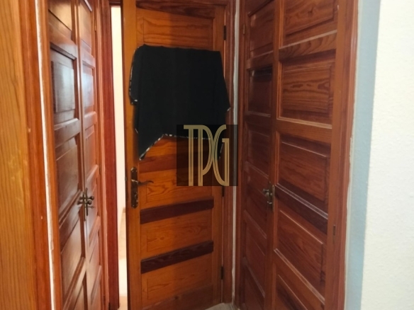 Narrow hallway with dark wood paneled doors on both sides; a black garment hangs over the open door at the end.