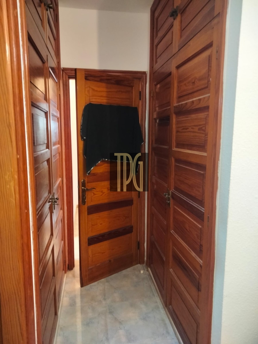 Narrow hallway with dark wood paneled doors on both sides; a black garment hangs over the open door at the end.