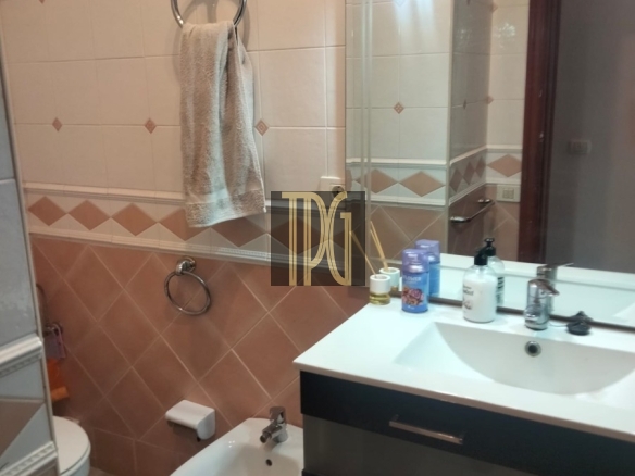 Bathroom with a white sink vanity, bidet, and toilet; towel hanging on circular metal rack and mirror above the sink.