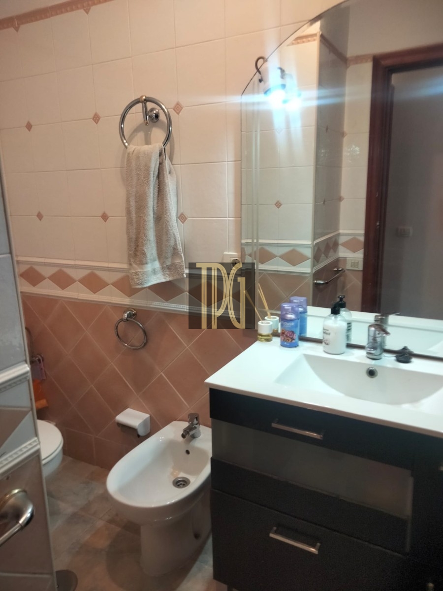 Bathroom with a white sink vanity, bidet, and toilet; towel hanging on circular metal rack and mirror above the sink.