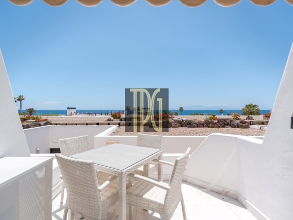 White wicker patio table and chairs on a sunlit terrace overlooking the blue sea and sky.