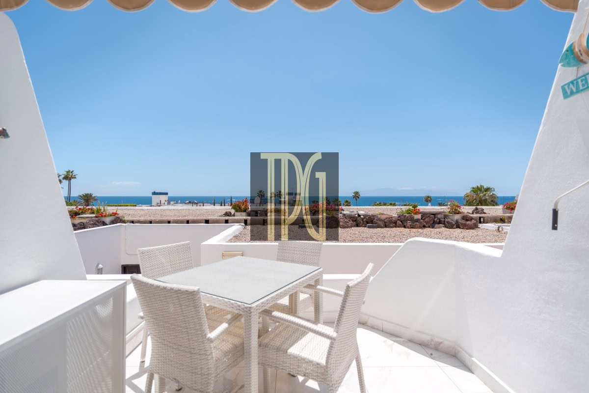 White wicker patio table and chairs on a sunlit terrace overlooking the blue sea and sky.