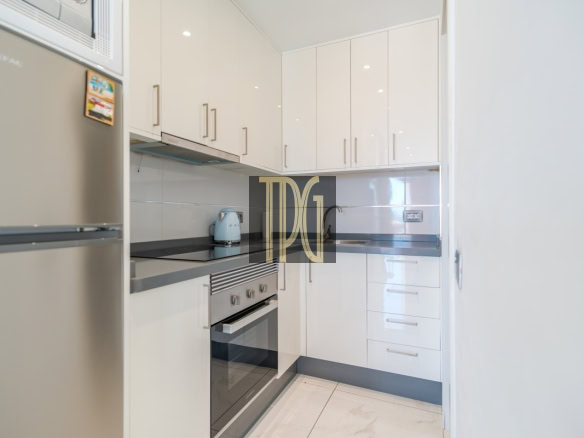 Compact white kitchen with glossy cabinets, stainless steel oven, gray countertops, and a turquoise kettle on the counter