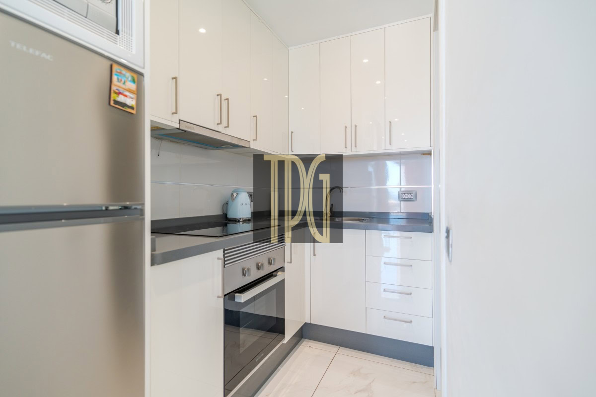 Compact white kitchen with glossy cabinets, stainless steel oven, gray countertops, and a turquoise kettle on the counter