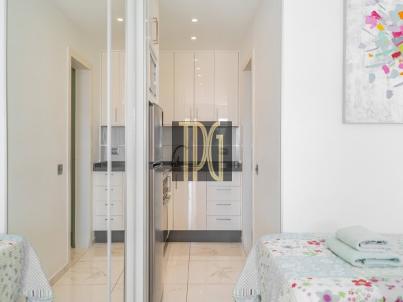 Bright white galley kitchen visible from a bedroom, with glossy cabinets and stainless steel appliances.