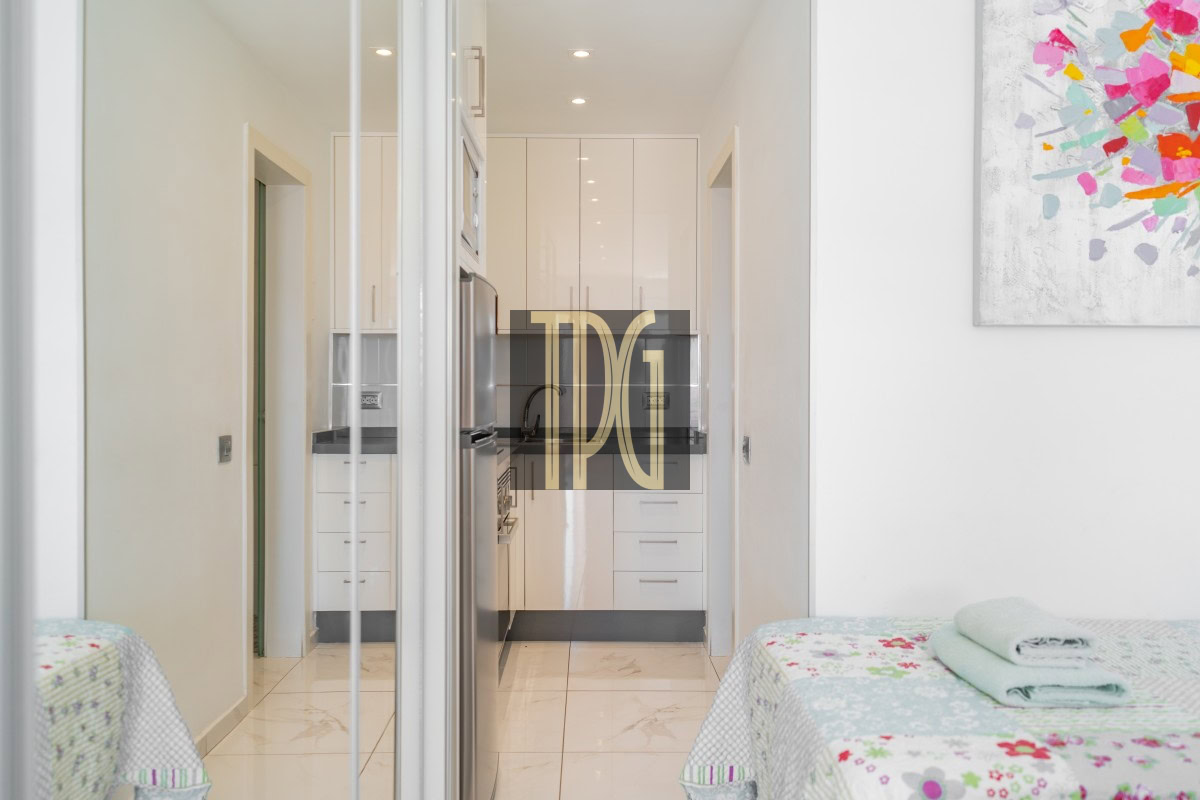 Bright white galley kitchen visible from a bedroom, with glossy cabinets and stainless steel appliances.