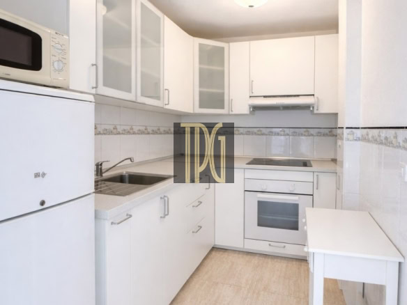 Bright white galley kitchen with white cabinets, microwave on the fridge, sink, oven, and a small white table.