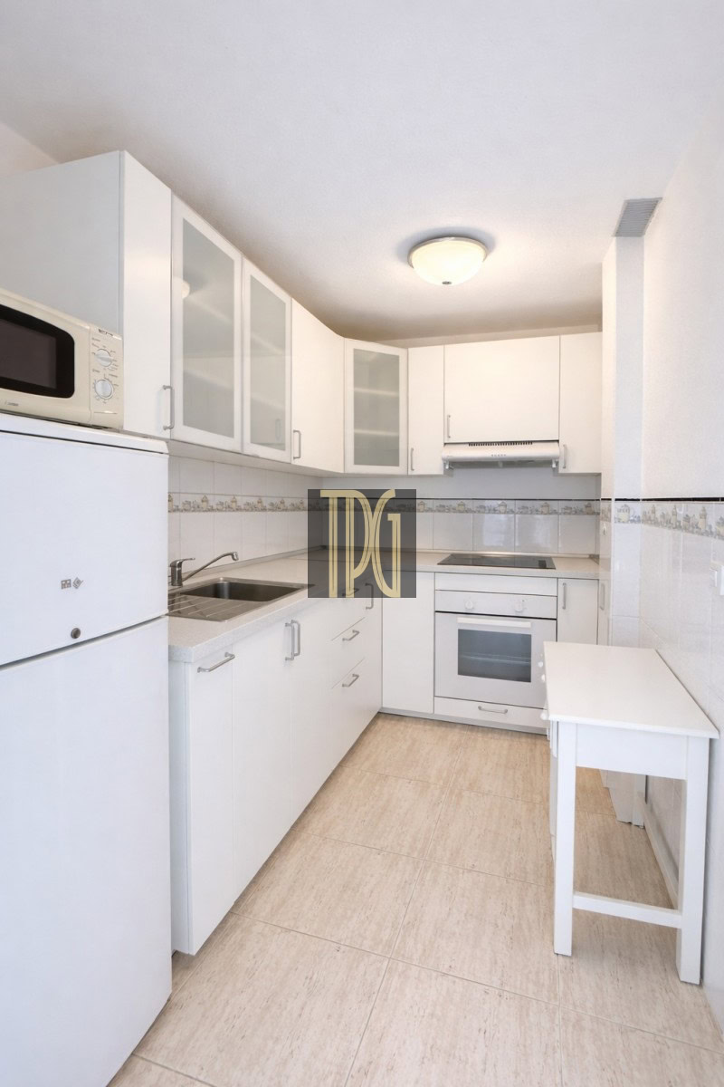 Bright white galley kitchen with white cabinets, microwave on the fridge, sink, oven, and a small white table.