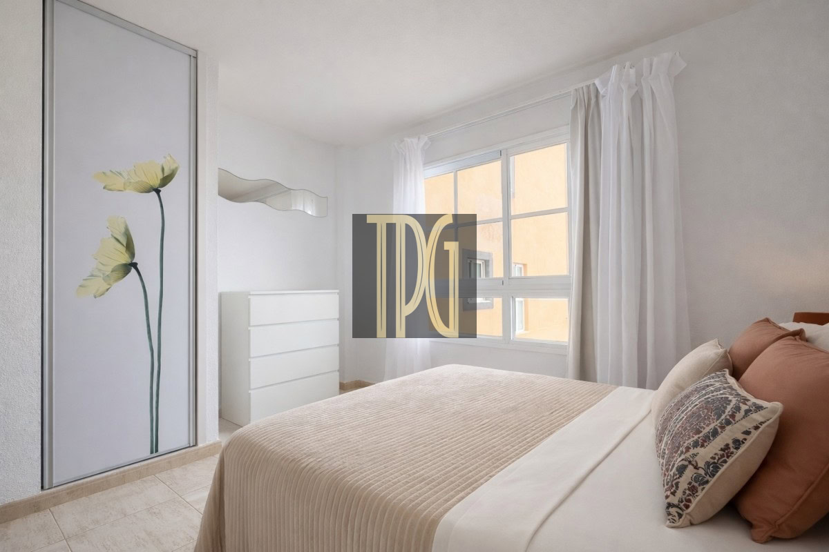Bright minimalist bedroom with white dresser, wavy mirror, and a sliding door with a floral panel in soft tones.
