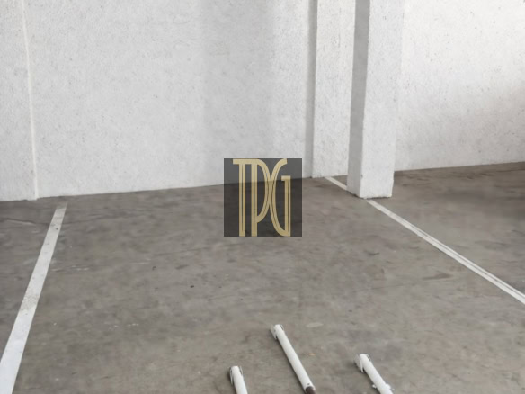 Empty indoor parking space with a white U-shaped pipe barrier on the floor and a ceiling light.