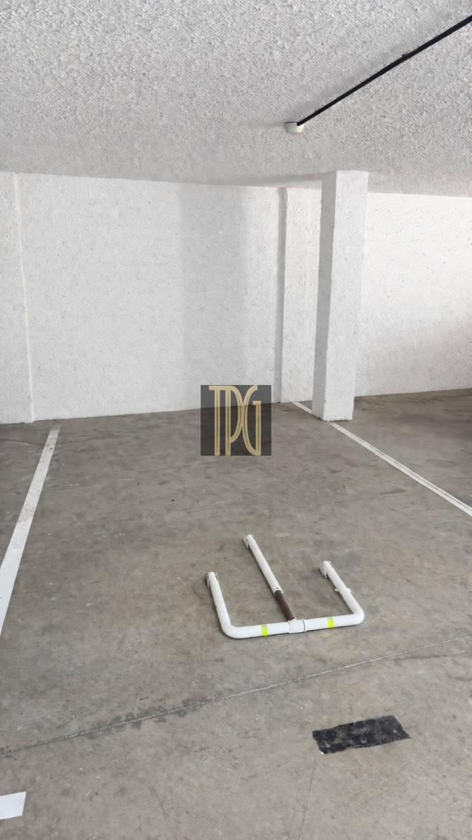 Empty indoor parking space with a white U-shaped pipe barrier on the floor and a ceiling light.